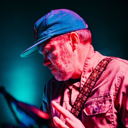 Scotty Nelson playing on stage, eyes down, in magenta and teal light